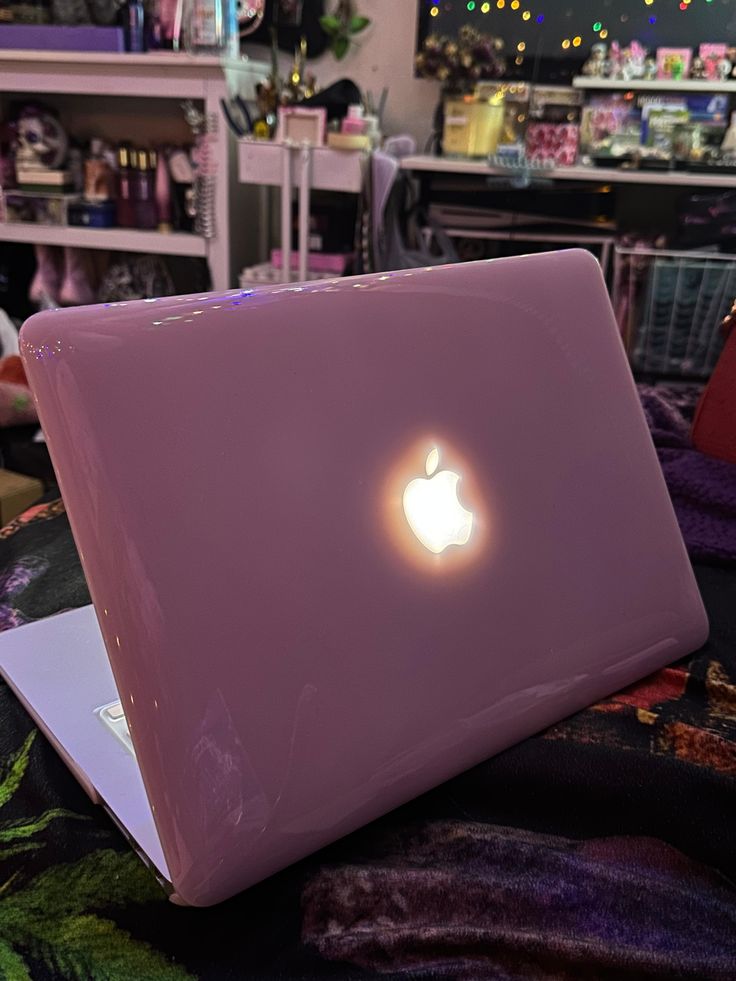 an apple laptop sitting on top of a bed in a room filled with other items