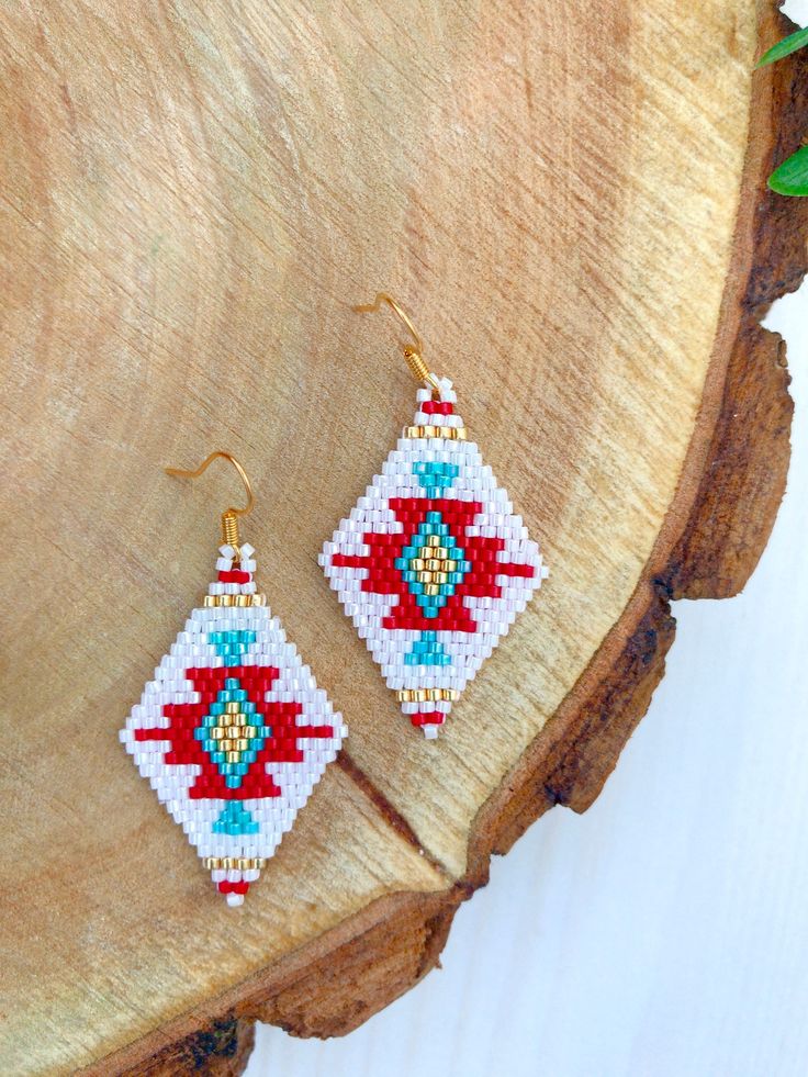 a pair of red and blue beaded earrings sitting on top of a piece of wood