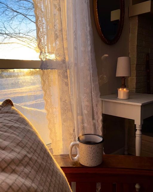 there is a coffee cup sitting on the window sill next to the bed in front of the window