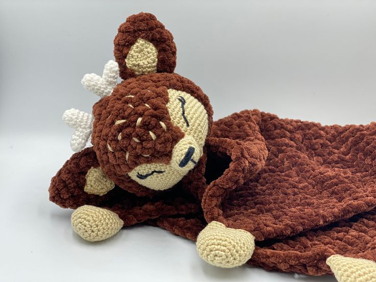 a crocheted brown and white stuffed animal laying on top of a blanket next to it's head