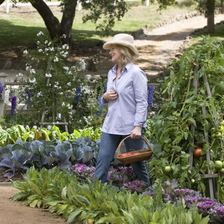 a woman walking through a garden carrying a basket