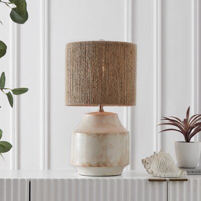 a white table with a lamp on it next to a potted plant and a sea urn