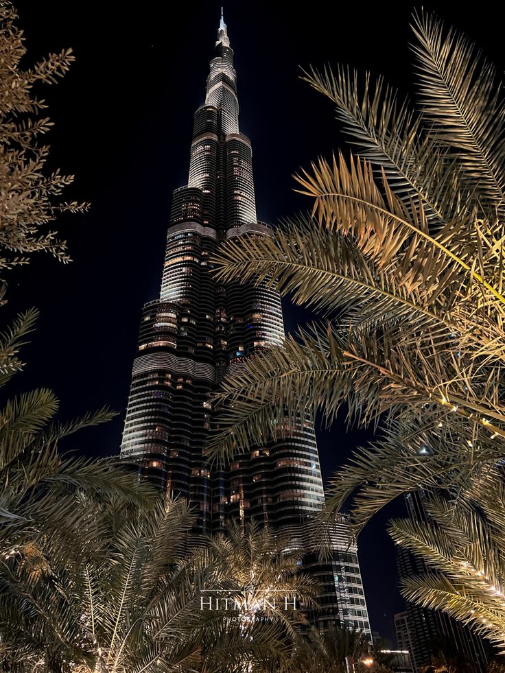 the burj building is lit up at night with palm trees in front of it