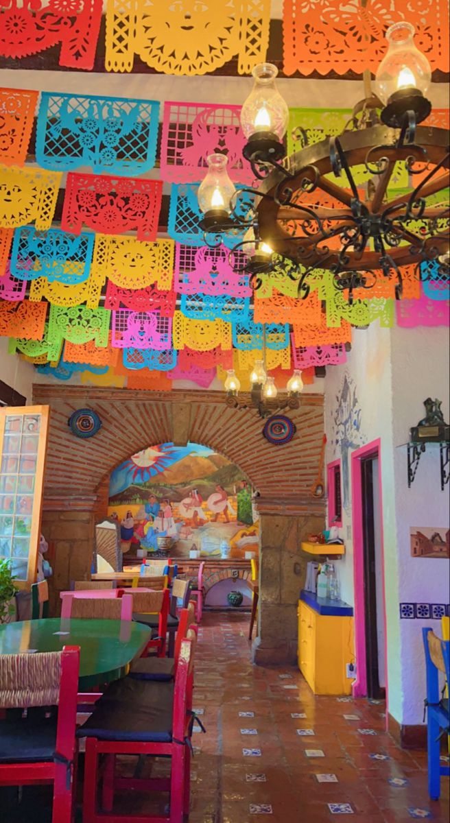 the interior of a mexican restaurant with brightly colored tables and chairs, decorated with paper cutouts