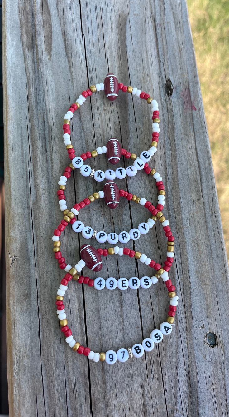 three bracelets with football beads and numbers on them sitting on a wooden plank in the grass