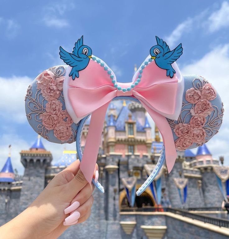 a hand is holding up a pink minnie mouse ears with blue and pink flowers on it