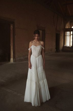 a woman standing in an empty room wearing a white dress with off the shoulder straps