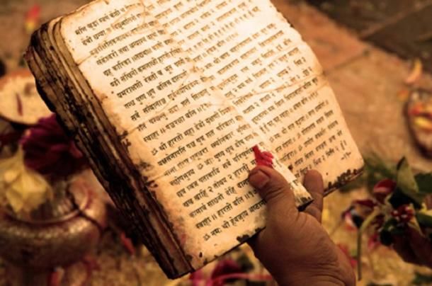 a person holding an old book in their left hand with writing on the pages and flowers around it