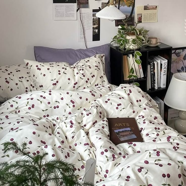 an unmade bed with white sheets and cherry print on it, next to a bookcase