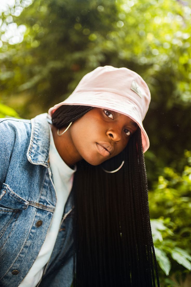 pink bucket hat on girl with long box braids and silver hoop earrings. wearing a denim jacket.