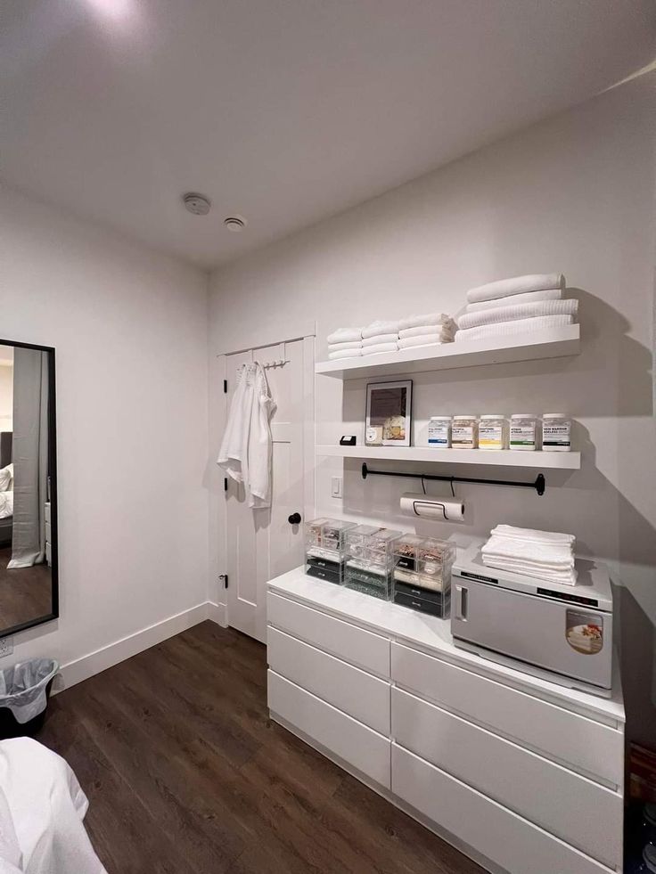 a bathroom with white cabinets and shelves filled with personal care items in front of a large mirror