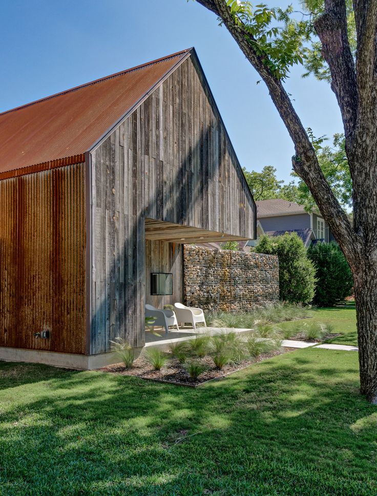 an old barn sits in the middle of a grassy area with trees and lawn furniture