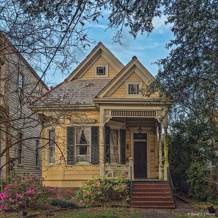 an old yellow house with flowers in the front yard and steps leading up to it