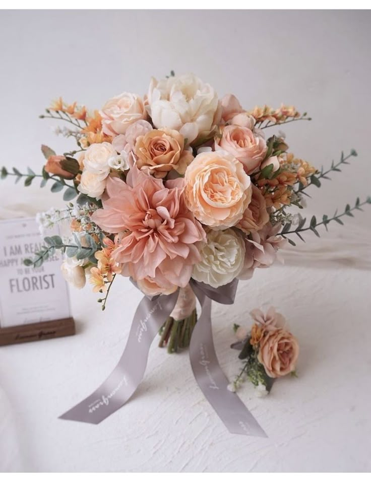 a bridal bouquet with peach and white flowers on a table next to a box of florist