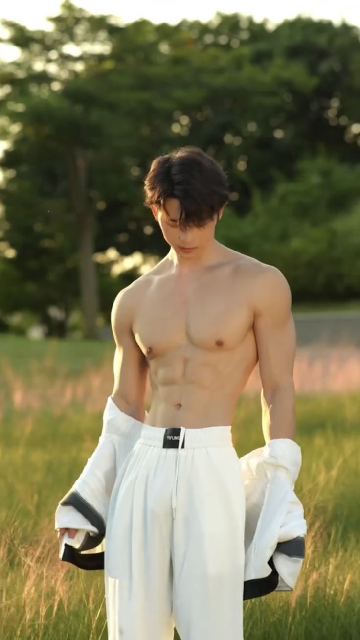 a shirtless man standing in the grass with his hands on his hips and wearing white pants