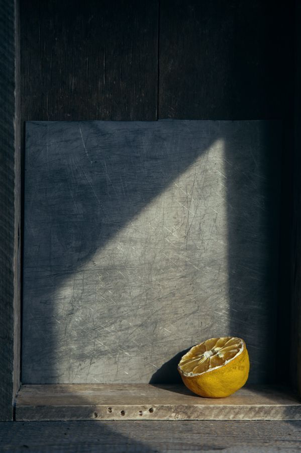 an orange sitting on top of a wooden shelf next to a window sill in a building