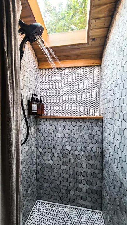 a shower head in the corner of a bathroom with tiled walls and flooring, under a skylight