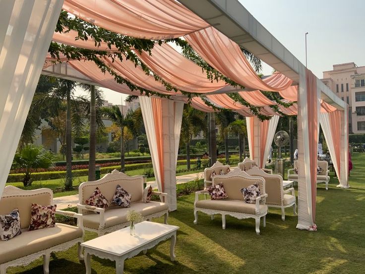 an outdoor area with couches, tables and drapes on the grass in front of buildings