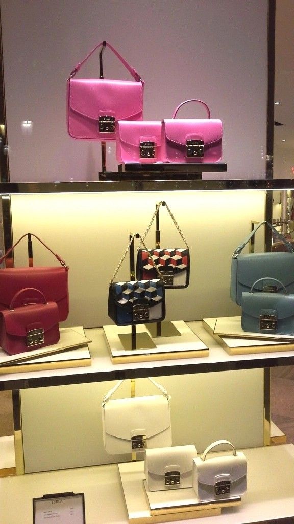 three different colored purses on display in a store window with other handbags behind them