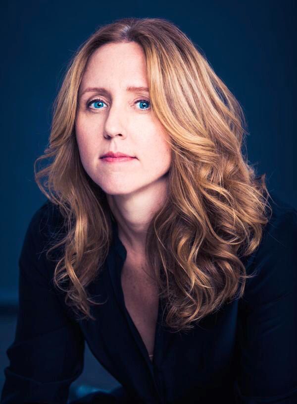 a woman with blonde hair and blue eyes posing for a photo in front of a dark background