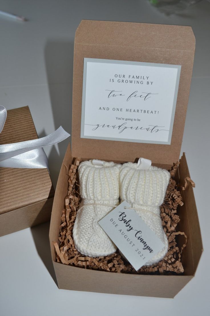 two baby booties in a gift box with a note on the tag that says, our family is growing by birth and one heartbeat