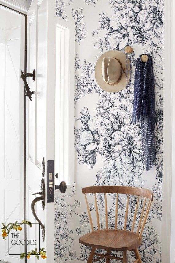 a hat is hanging on the wall next to a wooden chair in front of a floral wallpaper