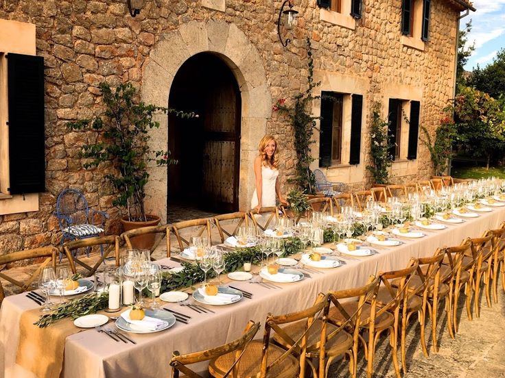 a long table with plates and glasses on it in front of an old stone building