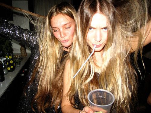 two young women standing next to each other holding drinks