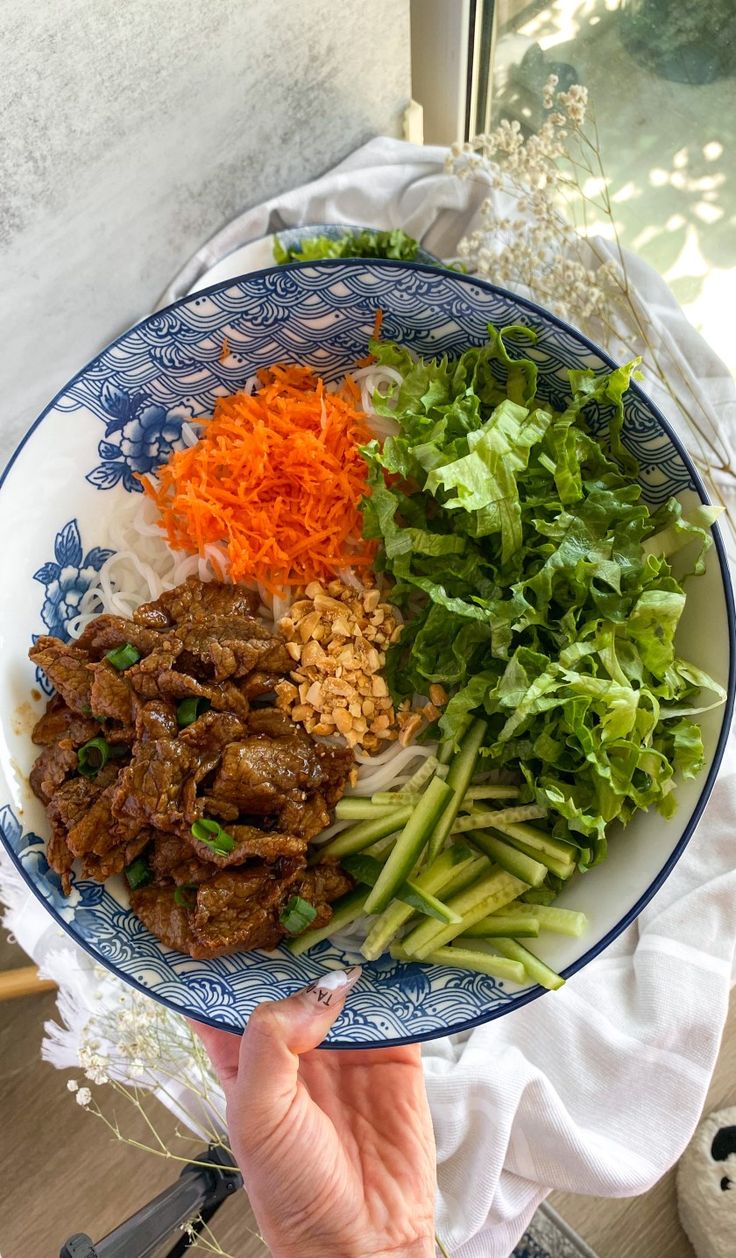 a blue and white plate topped with meat, veggies and rice next to a window