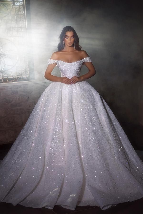 a woman in a white wedding dress standing by a window with her hands on her hips