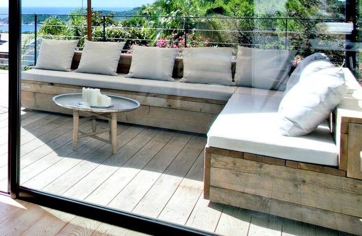 a couch sitting on top of a wooden floor next to a glass wall covered in white pillows