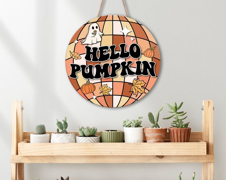 a hello pumpkin sign hanging from the side of a wall next to potted plants