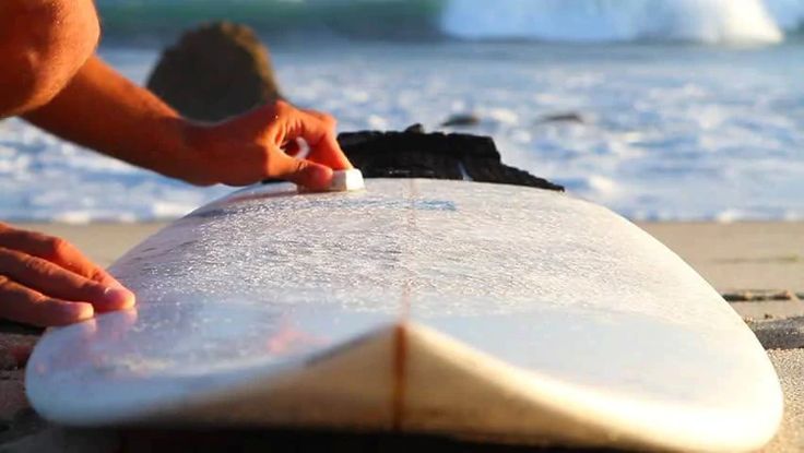 a man is waxing his surfboard on the beach