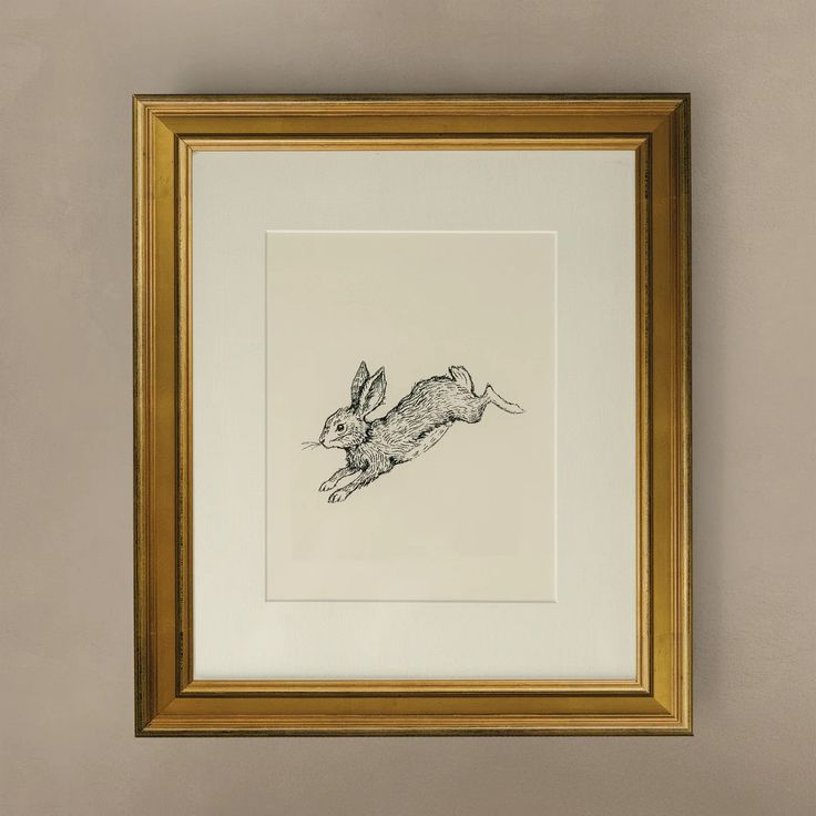 a black and white drawing of a rabbit in a gold frame hanging on the wall