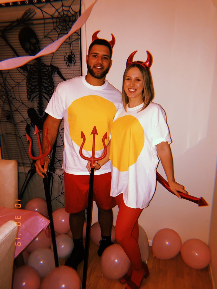 a man and woman dressed up as devil and demon with horns on their heads standing next to each other in front of balloons