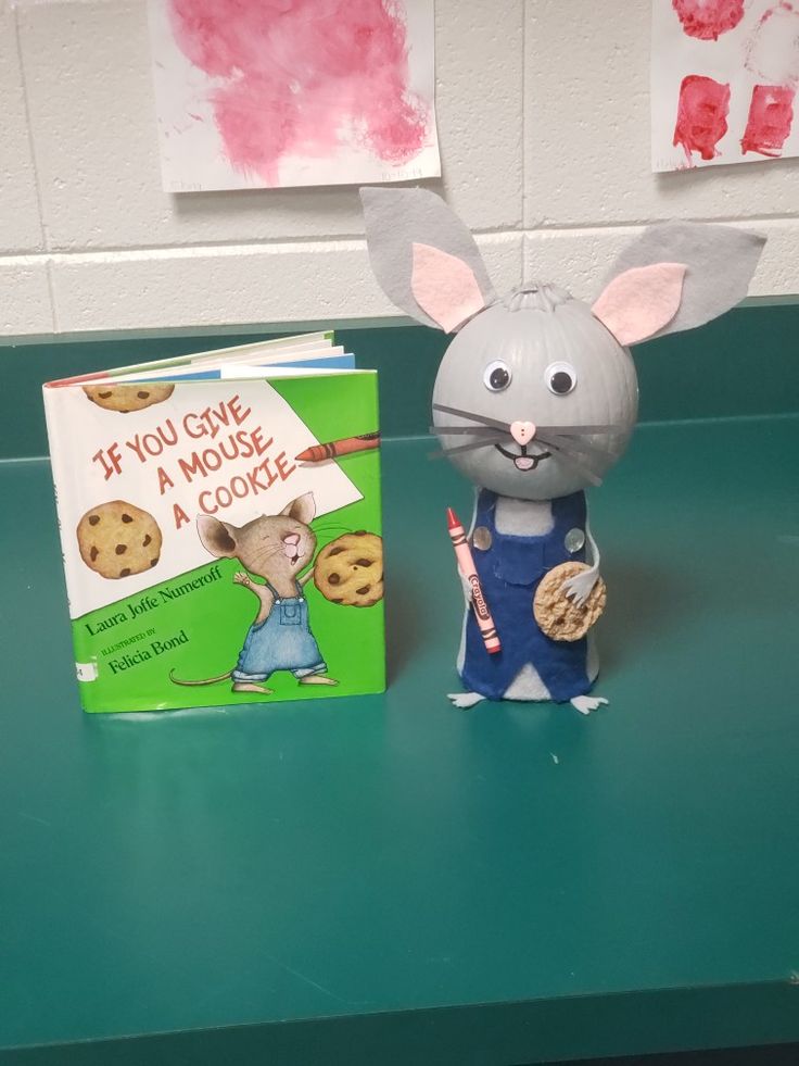 a book and toy mouse sitting on a green table next to a stuffed animal with a cookie in its hand