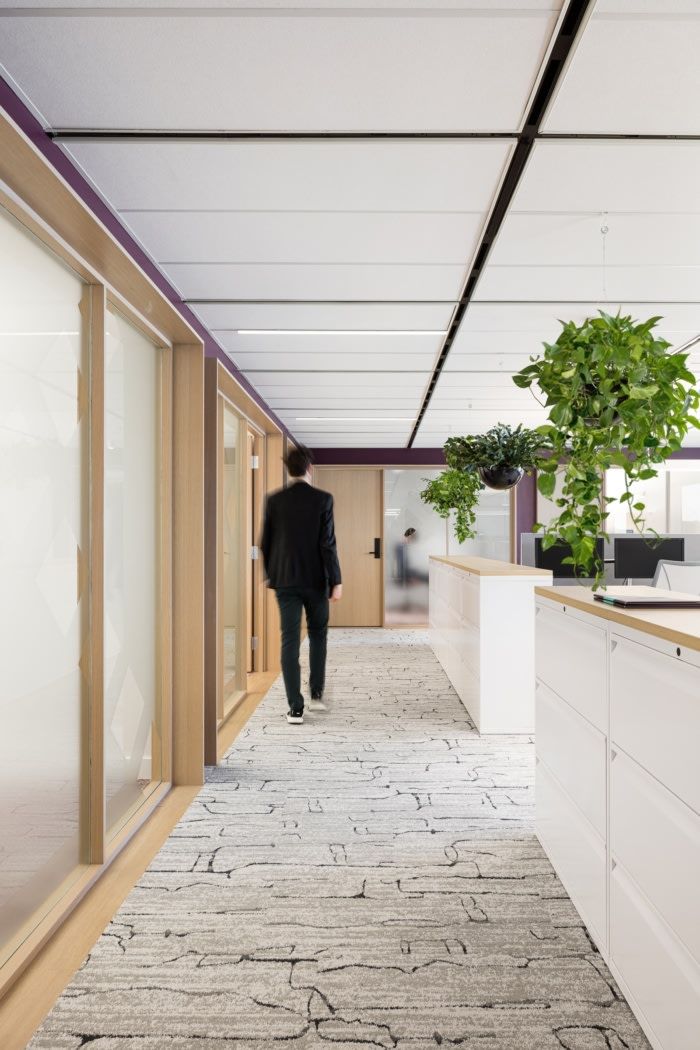 a man in a suit walking down an office hallway with plants on the wall and floor