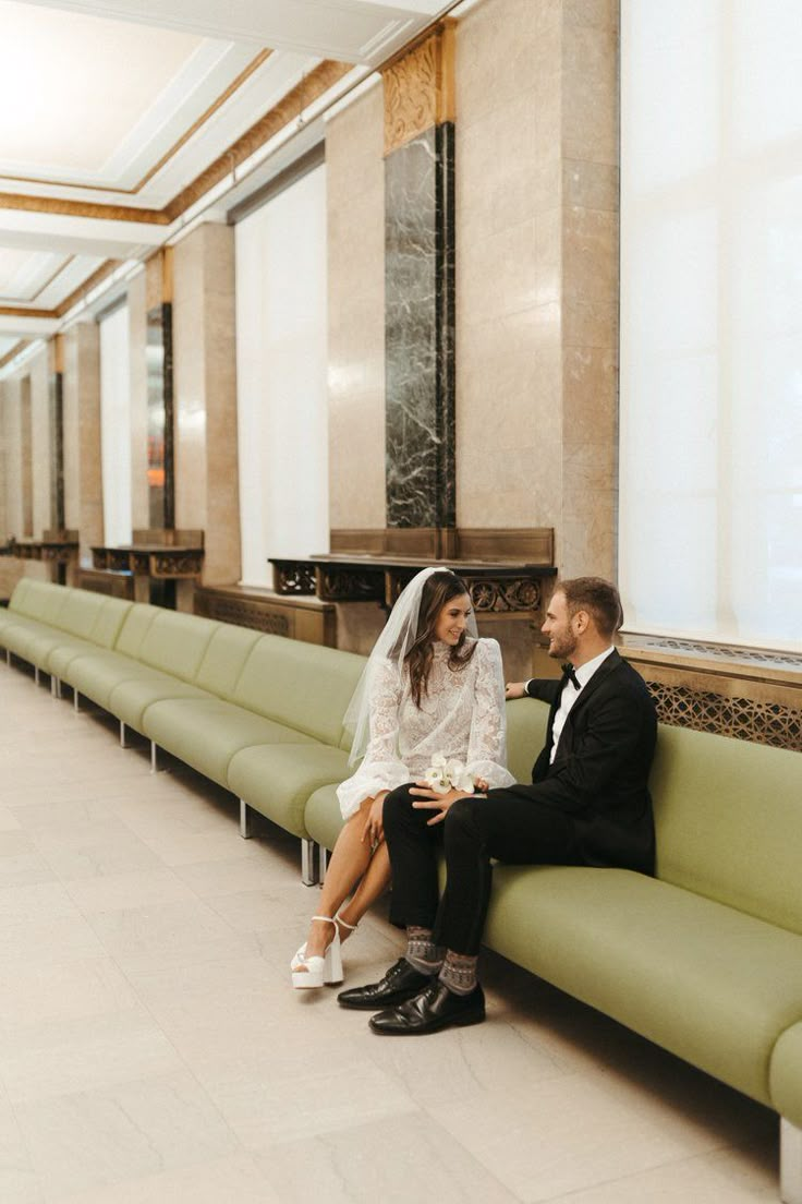 a bride and groom sitting on a green bench in the middle of a lobby area