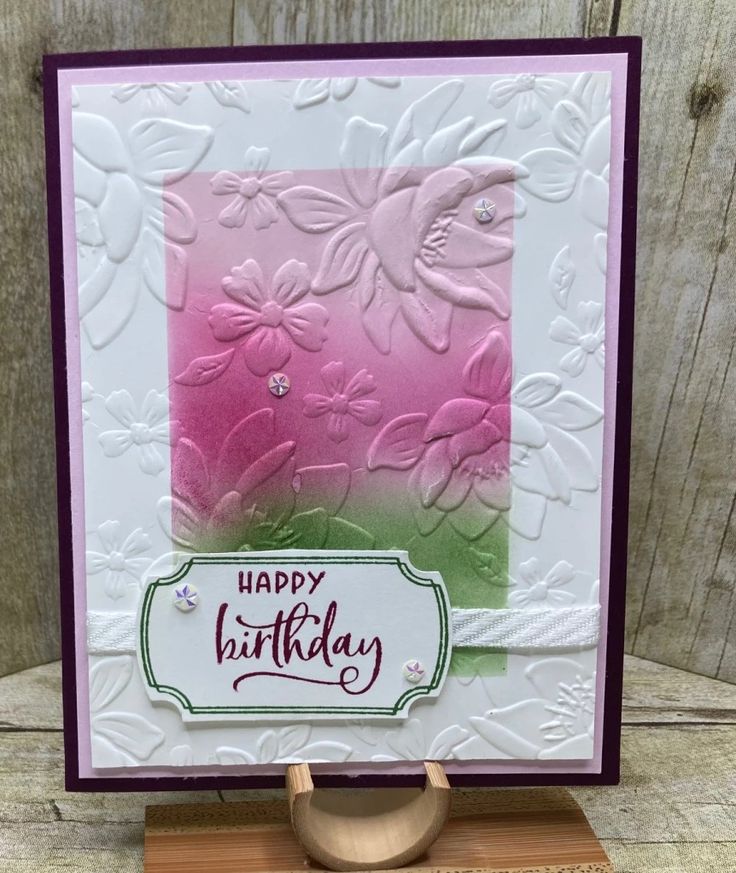 a happy birthday card with pink and green flowers on the front, sitting on a wooden stand