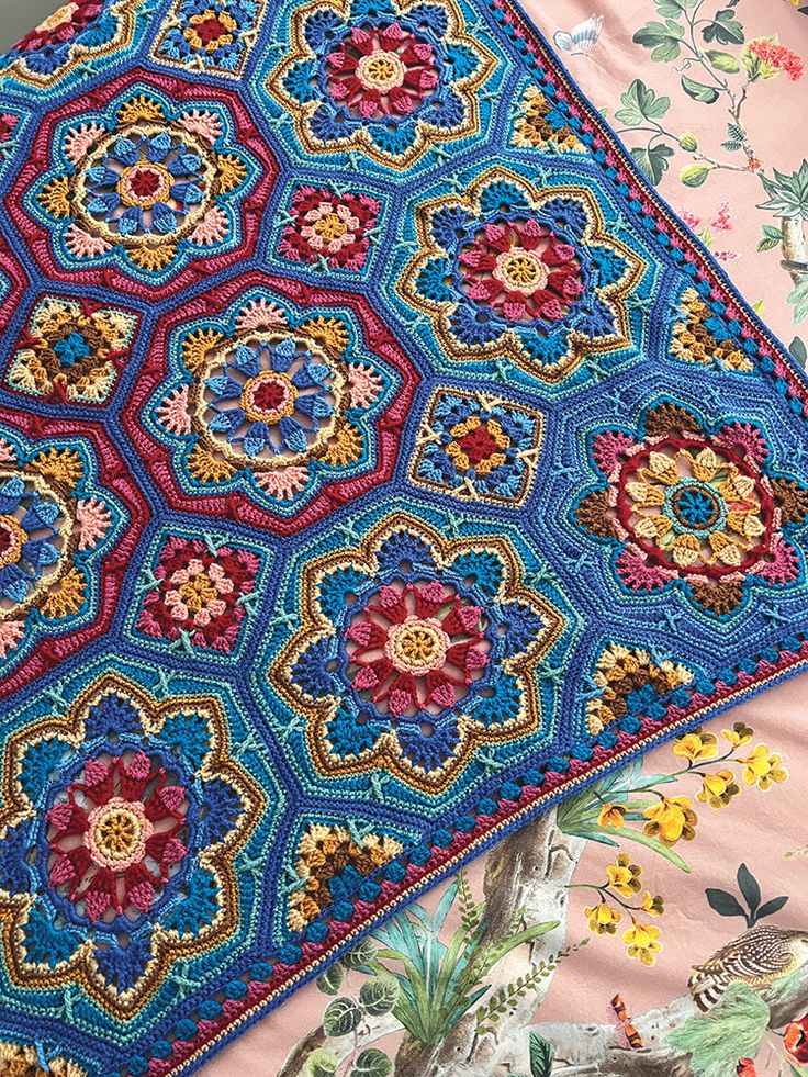 a colorful crocheted blanket on top of a bed covered in flowers and leaves