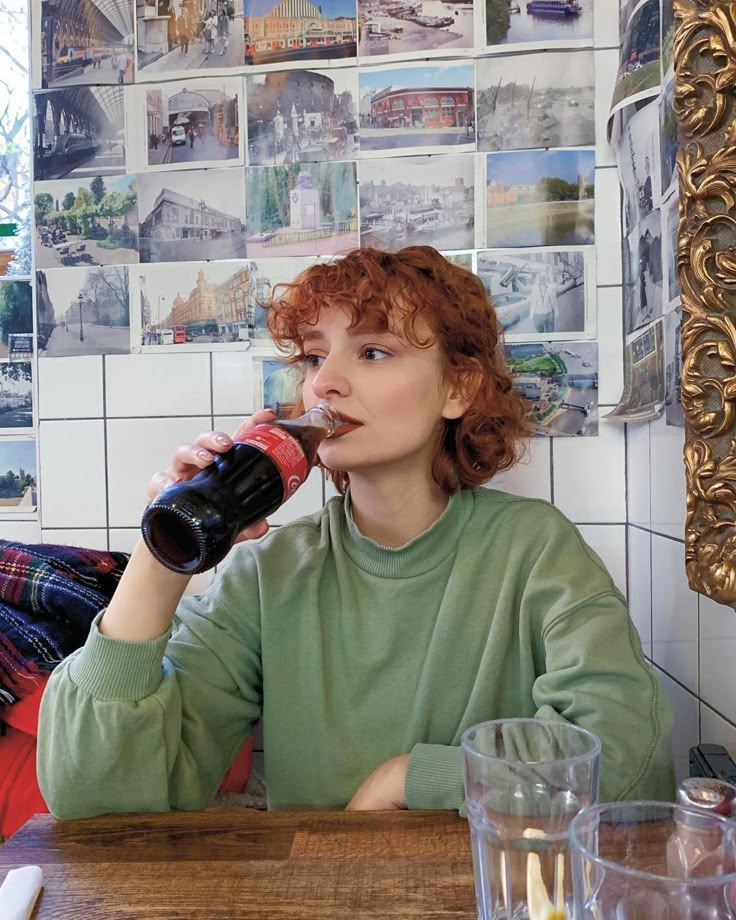 a woman sitting at a table drinking from a bottle