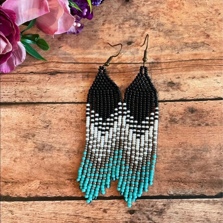 black and white beaded earrings with blue beads on wooden table next to purple flowers