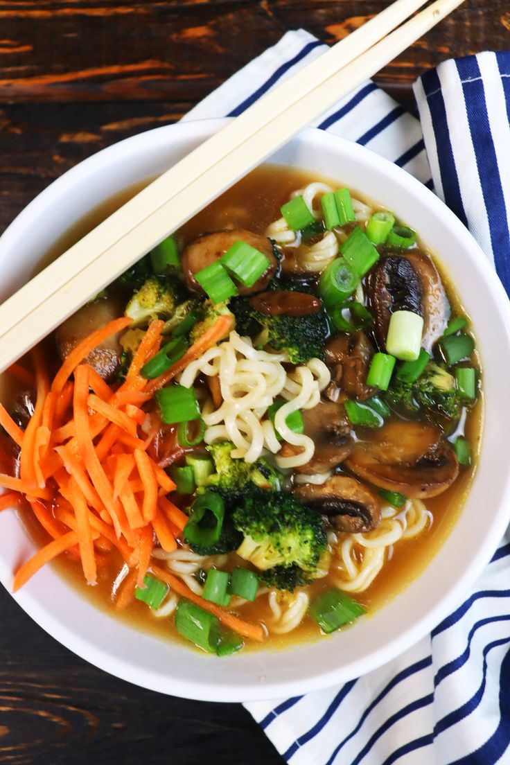 a white bowl filled with noodles, broccoli and carrots next to chopsticks