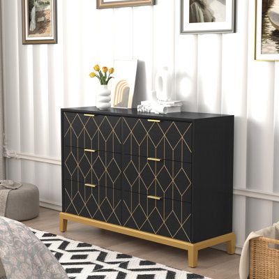 a black and gold chest of drawers in a living room with pictures on the wall