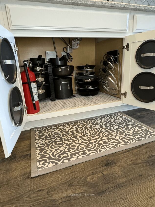 an open cabinet with pots and pans on the shelves next to a rug in front of it