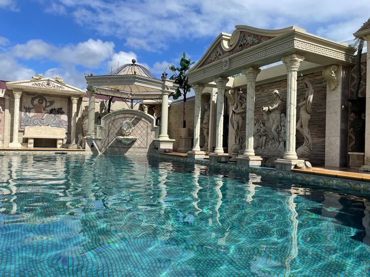 an outdoor swimming pool surrounded by columns and statues