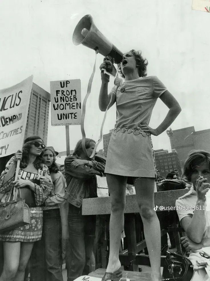 a woman speaking into a megaphone in front of a group of people holding signs