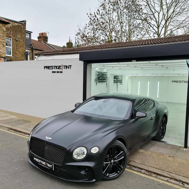 a black sports car parked in front of a white building on the side of the road