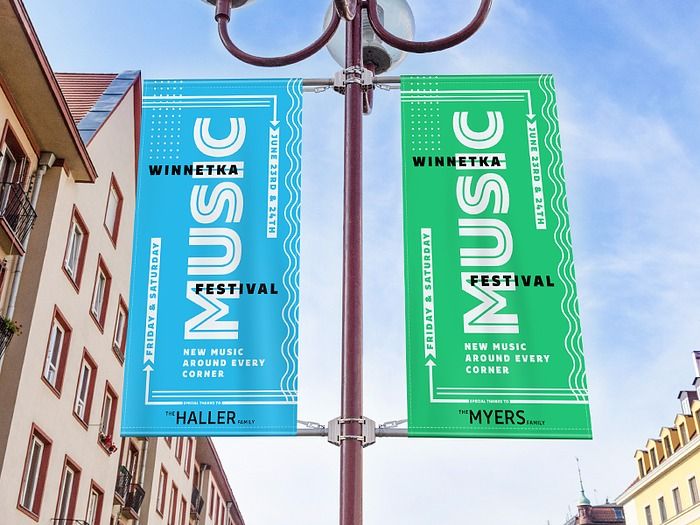 two banners are hanging from a street light in front of some buildings and trees on a sunny day