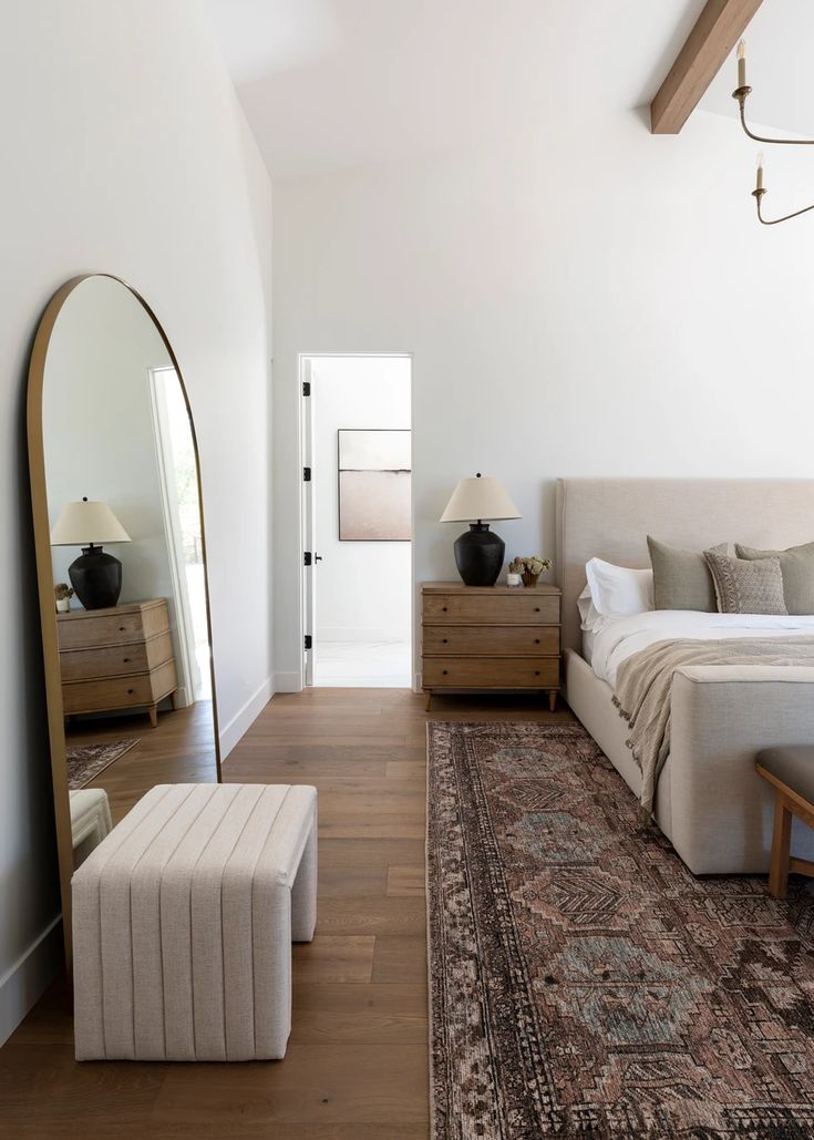 a bedroom with a bed, mirror and ottoman